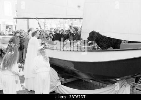 Couple marié Lambert scouts de mer en bateau devant le mariage de la mairie, Whizgle News, Dutch Desk, pays-Bas, 1950 - 2000 le 21-12-1983. L'image inclut ces rubriques. Dans un cadre animé de front de mer, un grand voilier occupe le devant de la scène, ses voiles blanches vives bouillonnant doucement comme si vous attrapiez une douce brise. La coque est peinte en bleu profond et blanc immaculé, contrastant magnifiquement avec les couleurs naturelles qui l'entourent. À bord du navire, un couple vêtu de vêtements blancs élégants et fluides capte l'attention, dégageant un air de célébration. Leur tenue semble formelle mais fantaisiste, parfait Banque D'Images