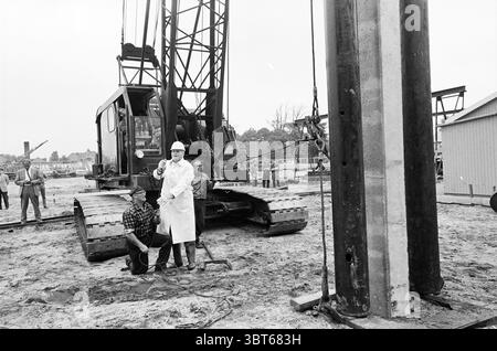 1ère ampoule perche premier pôle, Whizgle News, Dutch Desk, pays-Bas, 1950 - 2000 le 19-08-1969. Ce sont les éléments de l'image. La scène représente un chantier de construction animé par l'activité. Au centre de la composition se trouve une grande grue avec une structure robuste et une flèche proéminente, prête à soulever des matériaux lourds. Sa couleur métallique foncée contraste fortement avec l'environnement environnant. Au premier plan, deux individus sont placés en évidence. On est vêtu d'un costume de protection blanc et d'un casque de sécurité, debout avec confiance avec les mains sur les hanches, transmettant un sentiment d'autorité et d'excès Banque D'Images