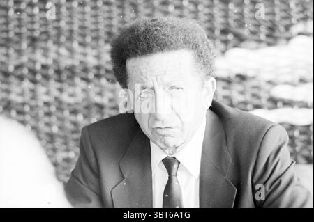 Mr. Orlandini KLM Amstelveen KLM Amstelveen, Whizgle News, Dutch Desk, pays-Bas, 1950 - 2000 on 20-08-1987. Voici les rubriques de l'image. La scène met en scène un homme plus âgé avec une coiffure distinctive caractérisée par une texture bouclée proéminente. Il semble porter une veste de costume sombre sur une chemise de couleur plus claire, complétée par une cravate qui ajoute de la formalité à son apparence. Son expression exprime un sentiment de sérieux ou de contemplation, avec des sourcils légèrement sillonnés et des lèvres bourrées, suggérant qu'il pourrait être profondément dans la pensée ou engagé dans une discussion sérieuse. L'arrière-plan est Banque D'Images