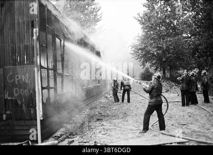 Asia Road School Fire brigade Haarlem Aziëweg pays-Bas, Whizgle News, Dutch Desk, pays-Bas, 1950 - 2000 on 18-08-1982. Ces rubriques sont illustrées dans l'image. La scène représente un effort dramatique de lutte contre l'incendie dans une zone boisée. Au premier plan, un pompier, vêtu d'un équipement de protection et d'un casque, dirige un puissant jet d'eau d'un tuyau épais vers une structure en feu. L'intensité du jet d'eau crée un nuage de brouillard et de vapeur, qui obscurcit partiellement la vue sur le bâtiment carbonisé derrière. Le bâtiment lui-même est dans un état de délabrement, avec du bois noirci Banque D'Images