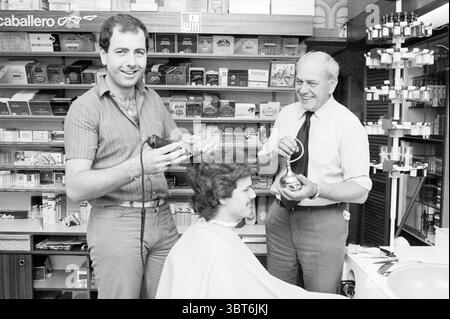 Coiffeur Zonneveld 70 ans anniversaire. Heemskerk coiffeurs et salons de coiffure Heemskerk, Whizgle News, Dutch Desk, pays-Bas, 1950 - 2000 le 02-09-1982. Ces rubriques sont illustrées dans l'image. Dans un salon de coiffure animé, deux hommes se tiennent à côté d'un client assis, qui a une cape de cheveux drapée autour d'eux. Le premier homme, avec une expression joyeuse, tient une tondeuse à cheveux près de la tête de son client, mettant en vedette une coiffure brun clair qui est en train d'être toilettée. Il est habillé d'une chemise rayée à manches courtes dans des tons froids de bleu et de gris, dégageant une ambiance détendue et professionnelle. A côté de lui, un ancien Banque D'Images