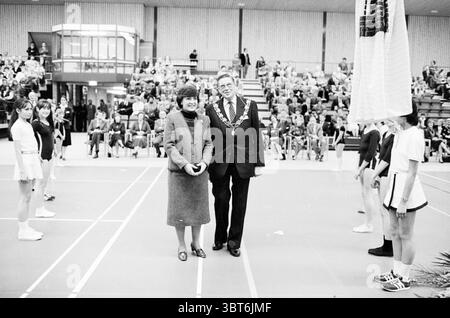 Ouverture de la salle d'événements Noordwijkerhout par Princess Margriet réceptions royales et visites royales ouverture ouverture commande Noordwijkerhout, Whizgle News, Dutch Desk, pays-Bas, 1950 - 2000 le 22-01-1982. L'image inclut ces rubriques. La scène capture un événement sportif officiel en salle, animé d'anticipation et de camaraderie. Au premier plan, deux personnages centraux se tiennent debout, dégageant un sentiment de fierté et de chaleur. La femme à gauche est élégamment habillée d'un manteau sombre et ajusté, sa coiffure soignée et polie. À côté d'elle, un homme est orné d'une tenue formelle, complète avec un c cérémonial Banque D'Images