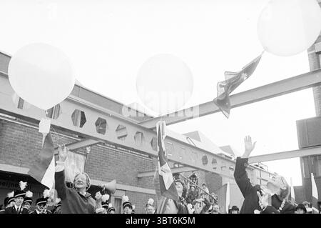 Groupes de musique de la Fête de la libération sur le Stationsplein à Haarlem Haarlem Stationsplein pays-Bas, Whizgle News, Dutch Desk, pays-Bas, 1950 - 2000 le 05-05-1980. Ce sont les éléments de l'image. Dans un cadre animé en plein air, un groupe de personnes est rassemblé sous un auvent, avec un accent sur deux individus qui lèvent les bras de manière bien visible. Ils célèbrent, peut-être lors d'une occasion festive. Au-dessus d'eux, de grands ballons ronds de couleur claire flottent gracieusement, ajoutant un sentiment de joie et de festivité à la scène. Les individus sont habillés en tenue festive, qui comprend coloré Banque D'Images