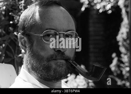 Henk van Dorp Pipe Smoking World Championships, Whizgle News, Dutch Desk, pays-Bas, 1950 - 2000 le 16-08-1993. Ces rubriques apparaissent dans l'image. La scène met en scène un homme avec une expression réfléchie, assis dans un cadre extérieur serein. Il a une barbe pleine et porte des lunettes rondes qui captent la lumière subtilement. Une longue pipe à fumer repose confortablement entre ses lèvres, lui donnant un comportement contemplatif. L'arrière-plan est rempli de verdure luxuriante, suggérant un jardin ou un parc, avec des ombres douces et tapissées jouant sur son visage. La lumière du soleil filtre à travers les feuilles, créant une chaleur et une tonicité Banque D'Images