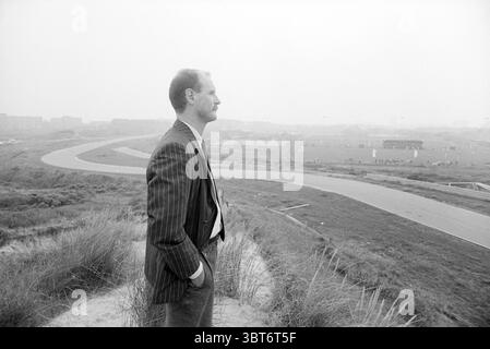 Visitez Z'voort '75, Whizgle News, Dutch Desk, pays-Bas, 1950 - 2000 le 02-10-1992. Ces rubriques apparaissent dans l'image. Dans cette scène, un homme se tient debout sur un boulevard herbeux surplombant une route sinueuse qui courbe à travers le paysage. Il est habillé d'un costume rayé, exsudant un sens de formalité et d'équilibre. Son profil est nettement défini par rapport aux éléments plus doux de l'arrière-plan, où la brume basse enveloppe la scène, créant une atmosphère éthérée. Les environs présentent un mélange d'éléments naturels et urbains. Vers la gauche, les zones d'herbe haute oscillent doucement dans une légère brise, tout en étant plus loin Banque D'Images