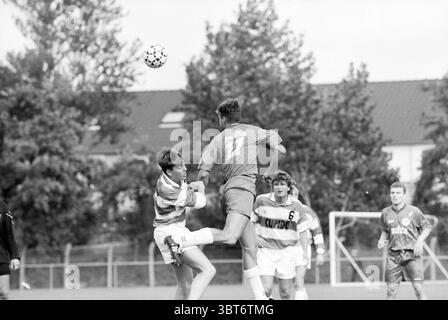 Dio - Haarlem, Whizgle News, Dutch Desk, pays-Bas, 1950 - 2000 le 03-09-1994. Voici les rubriques de l'image. La scène capture un moment intense sur un terrain de football. L'atmosphère est dynamique, mettant l'accent sur l'action du jeu. Un joueur portant un maillot rayé, peut-être blanc et bleu clair, tente de se défendre contre un adversaire qui saute gracieusement, portant une chemise grise avec un numéro dans le dos. L'action suggère une balle contestée, indiquant un esprit de compétition. Entourant les joueurs, le terrain est vivant avec des taches d'herbe verte, légèrement boueuse peut-être en raison de récents Banque D'Images