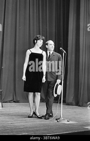 Cabaret Adam et Eve Cabaret, Whizgle News, Dutch Desk, pays-Bas, 1950 - 2000 le 04-03-1966. L'image contient ces rubriques. La scène met en scène deux individus debout ensemble sur une scène éclairée par un éclairage doux. Une personne, une femme, porte une robe noire simple mais élégante qui contraste avec son teint clair et ses cheveux foncés, qui est stylisée de manière chic. Elle semble prête, debout avec confiance, sa main gauche reposant sur sa hanche. A côté d'elle, un homme est habillé d'un costume sombre et d'une cravate légèrement plus légère, dégageant un charme professionnel. Il tient un chapeau de paille dans une main, qui Banque D'Images