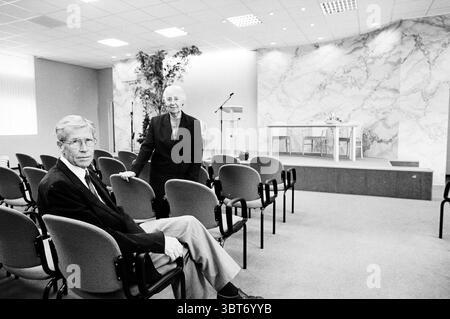Homme et femme dans la salle des témoins de Jéhovah Santpoort-Noord Vlietweg, Whizgle News, Dutch Desk, pays-Bas, 1950 - 2000 on 22-06-1997. L'image montre ces rubriques. La scène se déroule dans une salle spacieuse aménagée pour un rassemblement formel ou une présentation. Les murs arborent un design élégant et marbré dans des tons doux de beige et de crème, contribuant à un air d'élégance. Un éclairage lumineux et uniforme remplit la pièce, créant une atmosphère bien éclairée qui améliore la luminosité globale. Au premier plan, deux individus sont assis sur des chaises simples et modernes disposées dans une formation soignée. Une personne s'assoit avec un léger Banque D'Images