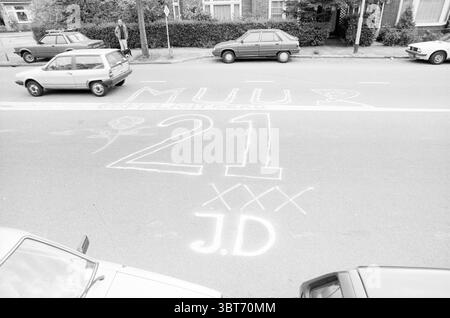 Texte d'anniversaire peint sur le Verspronckweg textes Haarlem Verspronckweg pays-Bas, Whizgle News, Dutch Desk, pays-Bas, 1950 - 2000 le 06-06-1988. L'image montre ces rubriques. La scène représente une rue urbaine animée, caractérisée par une variété de véhicules stationnés dans différents états de condition. Le premier plan est dominé par deux voitures compactes, toutes deux montrant des signes d'usure et d'âge, garées près du bord de la route. Leurs palettes de couleurs comprennent des nuances délavées de gris et de blanc, contribuant à un sentiment général de nostalgie. Au milieu de la rue, marquages craie blancs audacieux cre Banque D'Images