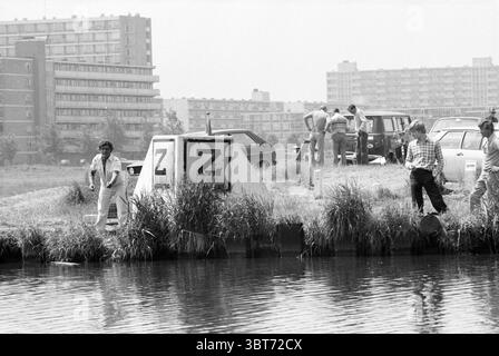 Pêche Wao'ers pêcheries et autres pêcheurs pêche, Whizgle News, Dutch Desk, pays-Bas, 1950 - 2000 le 05-07-1979. L'image montre ces rubriques. La scène capture un front de mer urbain animé par temps clair, avec la lumière du soleil illuminant la zone. Au premier plan, un petit groupe d'individus est engagé dans diverses activités près du bord de l'eau. Une personne, vêtue de vêtements légers, se tient à côté d'une grande structure en béton marquée de deux lettres proéminentes. Ils semblent examiner quelque chose dans l'eau. À proximité, un autre individu, portant une chemise à carreaux, regarde également Banque D'Images