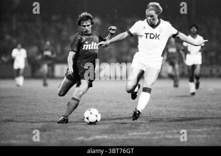 Football Haarlem - Ajax, Whizgle News, Dutch Desk, pays-Bas, 1950 - 2000 sur 09-1983. Ces rubriques apparaissent dans l'image. La scène capture un moment dynamique sur un terrain de football pendant un match. Deux joueurs sont en vedette, engagés dans une poursuite intense du ballon. Un athlète porte un maillot de couleur foncée, contrastant fortement avec l'uniforme blanc de l'autre joueur. Le joueur en blanc semble faire un jeu agressif, se penchant en avant alors qu'il tente de prendre le contrôle du ballon. L'herbe du terrain est bien entretenue, visible malgré le mouvement flou des joueurs. An Banque D'Images