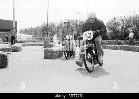 Solex race Rijsenhout cyclomoteurs riders cyclomoteurs Rijsenhout, Whizgle News, Dutch Desk, The Netherlands, 1950 - 2000 sur 14-06-1987. Ces rubriques sont illustrées dans l'image. Dans un cadre extérieur dynamique, deux coureurs sont engagés dans une course animée sur de petites motos. Le terrain est plat et pavé, bordé de balles de foin qui créent une limite et contribuent à une atmosphère rustique. Le jour semble couvert, projetant une lumière douce et diffuse qui donne à la scène une impression quelque peu vintage, accentuée par la qualité monochrome. Le premier coureur, portant un casque et une simple combinaison de course, se penche en avant, démontrant f Banque D'Images