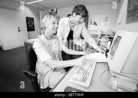 Deux dames A.W.V.N. Haarlem Westelijke Randweg pays-Bas, Whizgle News, Dutch Desk, pays-Bas, 1950 - 2000 le 28-05-1997. Ces rubriques apparaissent dans l'image. La scène représente un environnement de bureau animé caractérisé par une esthétique moderne, mais légèrement datée commune dans les espaces de travail. Deux individus sont engagés dans un moment de collaboration. Une personne, assise à un bureau, a une coupe de cheveux courte et élégante avec des brins de gris et est habillée dans une tenue beige clair. L'autre personne, debout à côté d'elle, a les cheveux plus foncés coiffés soigneusement et porte une veste blanche décontractée sur une chemise plus légère. Leur e Banque D'Images