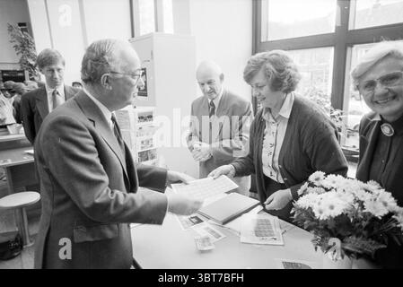 Timbres pour enfants Heemstede (vente de timbres dans le bureau de poste) Heemstede pays-Bas, Whizgle News, Dutch Desk, pays-Bas, 1950 - 2000 le 06-11-1990. L'image inclut ces rubriques. La scène capture un moment d'interaction dans un espace intérieur lumineux et bien éclairé. Un groupe de quatre individus se réunit autour d'une table, engagés dans la conversation. Au premier plan, un homme en costume, se distinguant par ses lunettes et un léger sourire, se penche en avant, présentant un ensemble de documents ou d'objets à une femme directement en face de lui. Elle a les cheveux bouclés et est habillée d'un cardigan, paraissant concentrée et int Banque D'Images