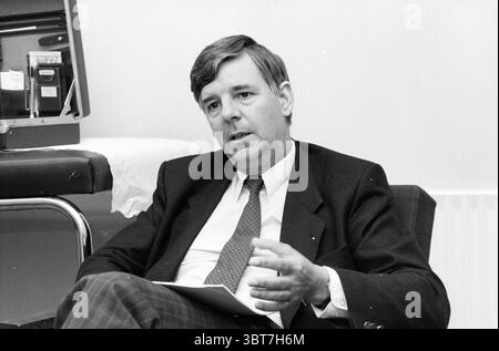 Mr. Lunshof M.S.D. M.S.d, Whizgle News, Dutch Desk, pays-Bas, 1950 - 2000 le 18-08-1987. L'image montre ces rubriques. Dans un cadre intérieur bien éclairé, un homme d'âge moyen s'assoit confortablement dans une chaise, penché légèrement en avant avec une expression engagée. Il est habillé d'un costume sombre classique avec un subtil motif à carreaux, complété par une chemise blanche et une cravate à motifs. Ses cheveux sont soigneusement stylisés, montrant un mélange de nuances sombres et grises, ajoutant une apparence distinguée. L'arrière-plan se compose d'un mur doux et de couleur claire, qui crée une atmosphère calme. D'un côté, il y a un sombre, St Banque D'Images