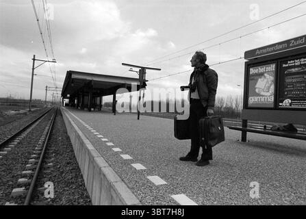 Man station Amsterdam-Zuid Station, Whizgle News, Dutch Desk, pays-Bas, 1950 - 2000 on 19-12-1978. Voici les rubriques de l'image. La scène capture un quai de gare marqué par un sentiment de solitude et d'anticipation. Une figure solitaire se tient sur la plate-forme, tenant deux valises sombres, une dans chaque main. La personne semble être d'âge mûr, vêtue de vêtements sombres qui se marient avec les tons discrets généraux du décor. L'expression sur leur visage suggère un mélange de contemplation et de préparation. Autour d'eux, la plate-forme est bordée de pierres lisses et grises, créant un contraste frappant A. Banque D'Images