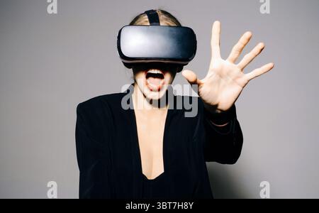 Femme portant des lunettes de réalité virtuelle. Jeu de réalité augmentée, technologie future. Fille étonnée dans des lunettes VR touchant quelque chose pendant l'expérience VR. V Banque D'Images