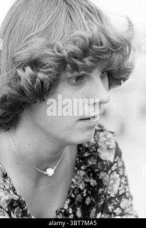 Portrait d'une jeune femme d'environ 30 ans., Whizgle News, Dutch Desk, pays-Bas, 1950 - 2000. L'image contient ces rubriques. La scène capture une jeune femme aux cheveux bouclés qui encadre son visage doucement. Ses cheveux sont de longueur moyenne, en cascade doucement autour de ses épaules avec un rebond vif. Elle a une expression sérieuse, avec ses lèvres légèrement écartées comme si elle était en pleine pensée ou conversation. Sa tenue présente un motif floral dans des tons sombres qui contraste magnifiquement avec sa peau claire. Les couleurs de ses vêtements suggèrent une ambiance vintage, avec des teintes vibrantes mais discrètes th Banque D'Images