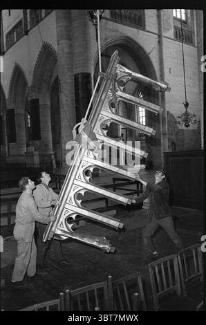 Hissage de la balustrade dans les églises Grote ou Sint-Bavokerk Grote Kerk Haarlem : Bavokerk Haarlem Grote Markt The Netherlands, Whizgle News, Dutch Desk, The Netherlands, 1950 - 2000 on 01-05-1968. L'image contient ces rubriques. Dans un grand espace intérieur caractérisé par des arches gothiques imposantes et un haut plafond, un groupe de trois individus est vu engagé dans un effort coordonné. Leurs expressions reflètent un mélange de concentration et de détermination, car elles soulèvent collectivement un grand meuble ou une parure architecturale au design complexe. L'objet hissé est Banque D'Images
