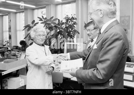 1ère présentation du permis de conduire dans la municipalité de Velsen Eerste Steen présentation Velsen, Whizgle News, Dutch Desk, pays-Bas, 1950 - 2000 le 30-09-1986. Voici les rubriques de l'image. Dans un environnement de bureau spacieux et bien éclairé, une femme âgée aux cheveux blancs bouclés et aux lunettes est engagée dans une poignée de main chaude. Elle porte une blouse de laboratoire de couleur claire, suggérant un comportement professionnel. Son expression rayonne de convivialité, complétée par un léger sourire. Un homme en costume pointu, avec des cheveux gris et des lunettes, se tient en face d'elle, souriant également en étendant sa main pour compléter les mains Banque D'Images
