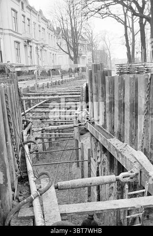 Ouvrages d'assainissement Parklaan Works Haarlem Parklaan pays-Bas, Whizgle News, Dutch Desk, pays-Bas, 1950 - 2000 on 15-12-1965. Voici les rubriques de l'image. La scène représente un chantier de construction actif encadré par une toile de fond d'architecture traditionnelle, caractérisée par des bâtiments élégants aux façades ornées bordant la rue. Ces structures, probablement résidentielles ou commerciales, comportent de grandes fenêtres et des moulures décoratives, suggérant un quartier riche. À l'avant-garde, une tranchée d'excavation traverse le centre, marquée par des étayages robustes en bois et en métal conçus pour maintai Banque D'Images