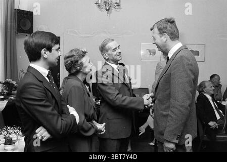 Adieu HR van Randwijk NZH Noord Zuid Hollandse Vervoersmaatschappij N.V. NZ, Whizgle News, Dutch Desk, pays-Bas, 1950 - 2000 on 23-05-1980. Ces rubriques apparaissent dans l'image. Dans un cadre intérieur spacieux avec un éclairage doux et silencieux, la scène capture un moment d'interaction cordiale entre plusieurs individus. Il y a quatre personnes bien en vue au premier plan, engagées dans une conversation qui transmet chaleur et familiarité. Sur la gauche, un jeune homme avec une coiffure soignée et des lunettes se tient debout avec un léger sourire, portant un costume sombre complété par une cravate à motifs. Il apparaît à Banque D'Images