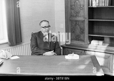 Portrait du nouveau maire Haarlemmerliede maires, Whizgle News, Dutch Desk, pays-Bas, 1950 - 2000 le 05-06-1968. Ce sont les éléments de l'image. La scène met en scène un homme bien habillé assis à un grand bureau en bois dans un cadre modeste de bureau. Il porte des lunettes sombres et un costume qui a une coupe classique, véhiculant un sens du professionnalisme et de l'autorité. Le bureau est épuré, avec seulement un petit gâteau rond reposant sur une assiette blanche devant lui, orné d'une seule bougie. Derrière lui, une armoire avec des sculptures en bois ornées se dresse contre le mur, mettant en valeur quelques b soigneusement disposés Banque D'Images