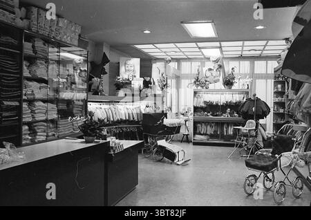 FA. Klein Cronjéstraat magasins et kiosques de vêtements pour enfants Haarlem Generaal Cronjéstraat pays-Bas, Whizgle News, Dutch Desk, pays-Bas, 1950 - 2000 le 02-10-1965. Voici les rubriques de l'image. La scène capture un espace de vente au détail confortable et bien organisé, probablement un magasin pour enfants. D'un côté, des serviettes et des couvertures soigneusement empilées sont disposées sur des étagères, leurs textures douces invitant à un sentiment de confort. Les couleurs de ces tissus semblent être atténuées, avec des pastels légers dominant la palette, suggérant chaleur et innocence. Au premier plan, un comptoir élégant et sombre offre un c Banque D'Images
