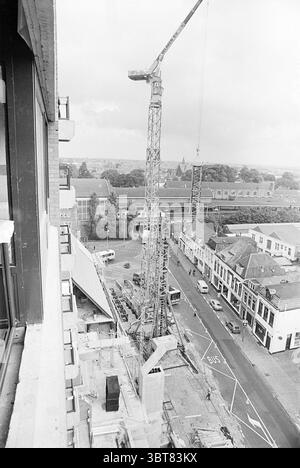 Construction Beijneshal Haarlem Jansweg pays-Bas ., Whizgle News, Dutch Desk, pays-Bas, 1950 - 2000. Ce sont les éléments de l'image. La scène met en valeur un environnement urbain animé, principalement axé sur un chantier de construction visible depuis un point de vue élevé. Au premier plan, une grande grue de construction domine le paysage, son bras tendu vers l'extérieur avec un gréement mécanique, suggérant des travaux actifs en cours. Autour de la grue, plusieurs matériaux de construction et équipements se trouvent dispersés. Les grands blocs de béton et les échafaudages font allusion aux efforts de construction en cours, Banque D'Images