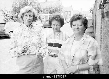 Maison de soins infirmiers Velserduin travail bénévole, Whizgle News, Dutch Desk, pays-Bas, 1950 - 2000 le 12-06-1987. Ces rubriques apparaissent dans l'image. La scène capture trois femmes debout ensemble par une journée ensoleillée, dégageant un sentiment de camaraderie. Chaque femme présente un style distinct qui reflète une combinaison d'élégance et de charme décontracté. La première femme sur la gauche porte une blouse fleurie avec un col haut et une jupe plissée, caractérisée par des couleurs pastel douces. Sa coiffure est volumineuse et stylisée en vagues lâches, ajoutant à son apparence sophistiquée. Elle tient une paire de lunettes dedans Banque D'Images
