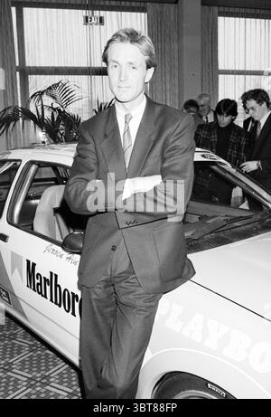 Portrait du pilote automobile Jeroen Hin en voiture., Whizgle News, Dutch Desk, pays-Bas, 1950 - 2000. L'image montre ces rubriques. Dans un cadre intérieur animé, un homme bien habillé se tient confiant à côté d'une voiture élégante ornée d'une marque frappante. Sa tenue se compose d'un costume sur mesure, avec une chemise blanche et une cravate, projetant un air de professionnalisme et d'équilibre. Il se penche légèrement contre le véhicule, dégageant un sentiment de confiance occasionnelle. La voiture elle-même dispose d'un design classique, et sa surface polie reflète des notes de l'éclairage chaud, attirant l'attention sur ses contours A. Banque D'Images