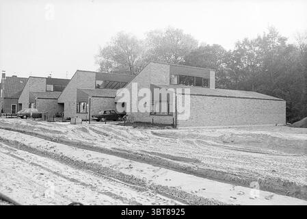 Maquette de maisons Lorentzlaan Heemstede, Whizgle News, Dutch Desk, pays-Bas, 1950 - 2000 en 1972. Ces rubriques sont illustrées dans l'image. La scène présente une rangée de maisons angulaires modernes, caractérisées par leurs toits plats et leurs formes rectangulaires. Les bâtiments sont construits à partir de briques de couleur claire, leur donnant un aspect propre et minimaliste. De grandes fenêtres permettent un aperçu des intérieurs, laissant entrer la lumière naturelle qui contraste avec les tons extérieurs discrets. Au premier plan, une zone sablonneuse s'étend sur la scène, indiquant des travaux de construction ou d'aménagement paysager. Chenilles de pneus tissées Banque D'Images