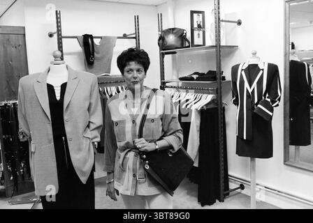 Mode féminine la Gonna Heemstede Heemstede pays-Bas, Whizgle News, Dutch Desk, pays-Bas, 1950 - 2000 sur 04-12-1997. L'image inclut ces rubriques. Dans une boutique de vêtements, la scène est centrée autour d'une femme, apparemment dans la trentaine. Elle a les cheveux courts et foncés soigneusement coiffés et porte un haut de couleur claire jumelé avec un pantalon blanc. La femme se tient confiante, tenant un sac à main noir sur son épaule. Son expression est calme et composée, faisant allusion à un sens du but. A sa gauche, un grand blazer sur mesure est accroché à un mannequin, son tissu gris doux contrastant avec la chaleur Banque D'Images