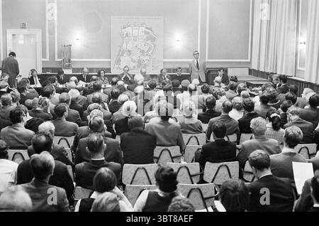 Teach-In City Center Meetings, Whizgle News, Dutch Desk, pays-Bas, 1950 - 2000 on 24-10-1969. L'image contient ces rubriques. La scène capture un grand rassemblement dans un cadre intérieur formel. Les rangées de chaises de couleur claire sont remplies d'un public diversifié, principalement des individus d'âge moyen et plus âgés, tous concentrés intentionnellement sur l'avant de la pièce. La foule est habillée dans un mélange de vêtements d'affaires, suggérant un événement professionnel ou communautaire. À l'avant, un groupe de personnes s'assoit derrière une longue table, engagé dans la discussion. Une personne se tient debout, s'adressant éventuellement au public, faisant des gestes Banque D'Images
