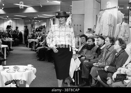 Défilé Van Vuuren Haarlem pays-Bas, Whizgle News, Dutch Desk, pays-Bas, 1950 - 2000 sur 31-01-1996. L'image montre ces rubriques. La scène capture un événement de mode animé qui se déroule dans un environnement de vente au détail spacieux, où un modèle marche en toute confiance sur une piste. Elle porte un ensemble audacieux composé d'une blouse à motifs avec des motifs géométriques et une jupe crayon noire classique, complétée par un chapeau élégant qui ajoute un élément de sophistication. Un public diversifié, composé principalement de personnes âgées, observe attentivement les rangées de petites tables ornées de délicates nappes. Banque D'Images