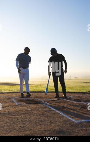 Divers coéquipiers masculins de baseball pratiquant dans la boîte de pâte sur le terrain avec casque de frappe et batte en métal Banque D'Images