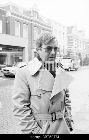 Portrait d'un homme pour le rapport 'électeurs à Zaandam Alkmaar et Beverwijk', Whizgle News, Dutch Desk, pays-Bas, 1950 - 2000 le 13-03-1978. L'image montre ces rubriques. La scène capture un cadre urbain avec un homme au premier plan, vêtu d'un trench-coat de couleur claire. Sa tenue vestimentaire suggère un environnement frais ou légèrement froid, complété par une écharpe enroulée autour de son cou. Il porte une paire de lunettes, et son expression semble réfléchie ou contemplative, faisant allusion à un dialogue interne. Autour de lui, le paysage urbain présente une rangée de bâtiments aux tons sourds, principalement en briques et Banque D'Images