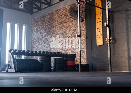 Porte-haltères contenant des haltères et des plaques de poids empilées dans un gymnase fonctionnel avec ventilateur industriel Banque D'Images