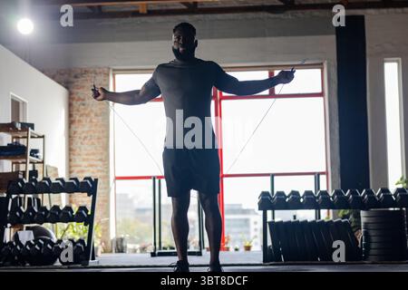 Homme afro-américain à la fin de la vingtaine à la corde à sauter dans un gymnase d'entrepôt converti portant des vêtements de sport Banque D'Images