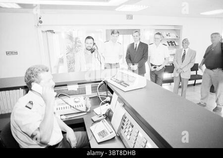 Mise en service du central téléphonique Hoofddorp police Hoofddorp pays-Bas, Whizgle News, Dutch Desk, pays-Bas, 1950 - 2000 on 28-07-1989. L'image contient ces rubriques. Dans une pièce bien éclairée, un groupe d'hommes se tient en demi-cercle, engagés dans la conversation. Le cadre semble être une zone de réception, avec un grand bureau de réception équipé de divers appareils, dont un téléphone et un clavier. Les hommes sont habillés dans un mélange de vêtements formels et décontractés. Un homme, assis au bureau, est en uniforme, concentré sur le téléphone, avec une expression sérieuse. Derrière lui, un trio d'hommes Banque D'Images