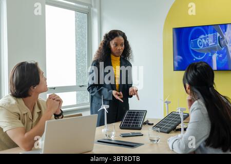 Divers collègues collaborant autour d'une table de conférence examinant les éoliennes et les panneaux solaires Banque D'Images