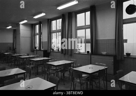 Blanc élect. Chauffage à Holland Plastic Haarlem sa zo Haarlem peintres P. de Vries IJmuiden chauffage, Whizgle News, Dutch Desk, pays-Bas, 1950 - 2000 on 17-02-1964. Ces rubriques apparaissent dans l'image. La scène représente une cafétéria spacieuse avec un design minimaliste. La salle est remplie d'une série de tables de couleur claire, disposées de manière ordonnée, chacune accompagnée de simples chaises en bois. Les tables présentent une surface lisse, éventuellement stratifiée, et sont parsemées de petits cendriers ronds. En arrière-plan, de grandes fenêtres dominent un mur, permettant à la lumière naturelle de s'infiltrer. Banque D'Images