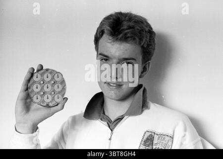 Marco Berkhout avec MRS Rubic puzzle IJmuiden Puzzle Jeux et jouets IJmuiden pays-Bas, Whizgle News, Dutch Desk, pays-Bas, 1950 - 2000 le 01-08-1988. Ces rubriques apparaissent dans l'image. Dans la scène, un jeune homme se tient confiant, présentant un disque circulaire tenu dans une main. Le disque est orné de plusieurs petits objets circulaires uniformes disposés soigneusement dans un motif en forme de grille. Chaque objet présente un design distinct qui attire le regard, suggérant une focalisation sur le détail et la précision. Le jeune homme a des cheveux clairs, légèrement bouclés, avec un teint jeune avec de légères taches de rousseur Banque D'Images