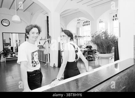 Bob van Wely ancien bureau de poste, Whizgle News, Dutch Desk, pays-Bas, 1950 - 2000 le 05-07-1994. L'image contient ces rubriques. Dans un intérieur spacieux et bien éclairé, deux individus partagent le focus de la scène. La salle dispose de hauts plafonds ornés de poutres en bois et de grandes fenêtres qui laissent entrer la lumière douce et naturelle. Des œuvres d'art encadrées et des photographies bordent les murs, améliorant l'atmosphère créative. À gauche, un homme se tient désinvolte appuyé contre un comptoir. Il a les cheveux bouclés et porte un t-shirt graphique qui ajoute un élément de jeu à son comportement. Son expression est amicale, wi Banque D'Images