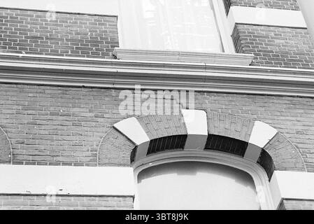 Bâtiments et fissures Schotersingel 117 Huizen Haarlem Haarlem Schotersingel pays-Bas, Whizgle News, Dutch Desk, pays-Bas, 1950 - 2000 on 27-01-1977. L'image contient ces rubriques. La scène présente un détail architectural d'un bâtiment, mettant l'accent sur une vue rapprochée d'une façade. La structure présente une combinaison de briques rouges et brunes, créant une texture riche. Les briques sont posées selon un motif traditionnel, entrecoupées de certaines zones qui présentent des signes d'usure, y compris des fissures et des surfaces inégales. Au sommet du mur, une arche distincte encadre une fenêtre, l'arche en alte Banque D'Images