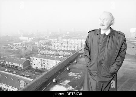 AB van Schooten regarde Schalkwijk et Vijfhuizen échevins, Whizgle News, Dutch Desk, pays-Bas, 1950 - 2000 le 01-12-1989. L'image inclut ces rubriques. La scène présente une figure debout bien en vue au premier plan, portant un long trench-coat sombre qui tremble légèrement dans la brise. Ils ont une expression réfléchie, regardant dans la distance au-delà du bord d'un toit. Les cheveux clairs de l'individu sont quelque peu touffus, contrastant avec leurs vêtements foncés. En arrière-plan, un paysage urbain tentaculaire se déploie, rempli d'un éventail de bâtiments résidentiels. Ces struct Banque D'Images