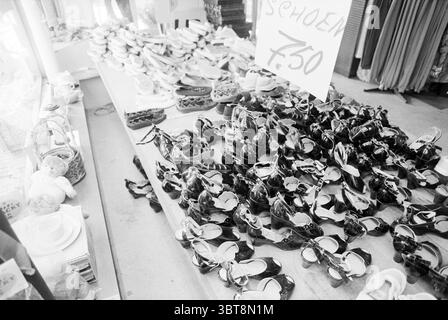 Intérieur tout est différent IJmuiden IJmuiden Nederland, Whizgle News, Dutch Desk, pays-Bas, 1950 - 2000 on 05-07-1993. L'image montre ces rubriques. La scène capture un étal de marché animé, débordant d'une variété de chaussures disposées en rangées ordonnées sur une table en bois. Les chaussures sont principalement noires, affichant différents styles, des simples mocassins aux types plus décoratifs avec des détails comme des noeuds et des embellissements. L'arrangement suggère un sentiment d'abondance, avec quelques paires semblant se bousculer pour attirer l'attention au milieu de l'exposition bondée. En arrière-plan, chaussures supplémentaires Banque D'Images