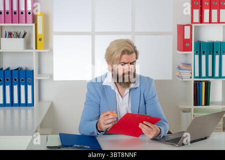 Inspecteur sérieux travaillant avec des dossiers papier presse-papiers et un ordinateur portable. Recherche d'informations commerciales. Rapports, documents. Auditeur masculin Banque D'Images