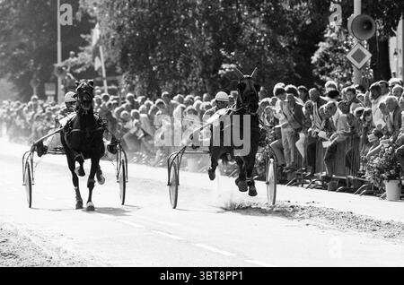 Course sur piste courte lisse et atmosphère trotting lisse, Whizgle News, Dutch Desk, pays-Bas, 1950 - 2000 le 25-09-1986. L'image montre ces rubriques. La scène capture une course de chevaux dynamique, avec deux chevaux tendus contre des harnais, leurs muscles puissants visibles alors qu'ils galopent sur une piste poussiéreuse. Les chevaux, l'un sombre et élégant et l'autre d'une teinte plus claire, montrent une concentration intense, leurs narines s'évasent et les yeux pointés vers l'avant. Les cavaliers vêtus d'une tenue blanche impeccable avec des casques s'assoient en toute confiance dans les sulkies derrière les chevaux, leurs postures se penchant en avant pour améliorer la vitesse. Poussières Banque D'Images