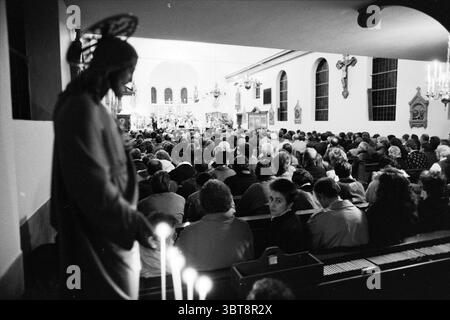 Service religieux RK Haarlemmerliede Churches, Whizgle News, Dutch Desk, pays-Bas, 1950 - 2000 on 24-12-1988. Voici les rubriques de l'image. La scène représente un intérieur bondé d'un lieu de culte, avec un nombre considérable de personnes rassemblées pour un service. L’atmosphère est solennelle et réfléchissante, amplifiée par un éclairage doux et chaleureux qui illumine doucement l’espace. À gauche, il y a une statue représentant une figure, probablement une icône religieuse, avec une expression sereine et des détails. La présence de la statue ancre la scène, contrastant avec la dynamique active Banque D'Images